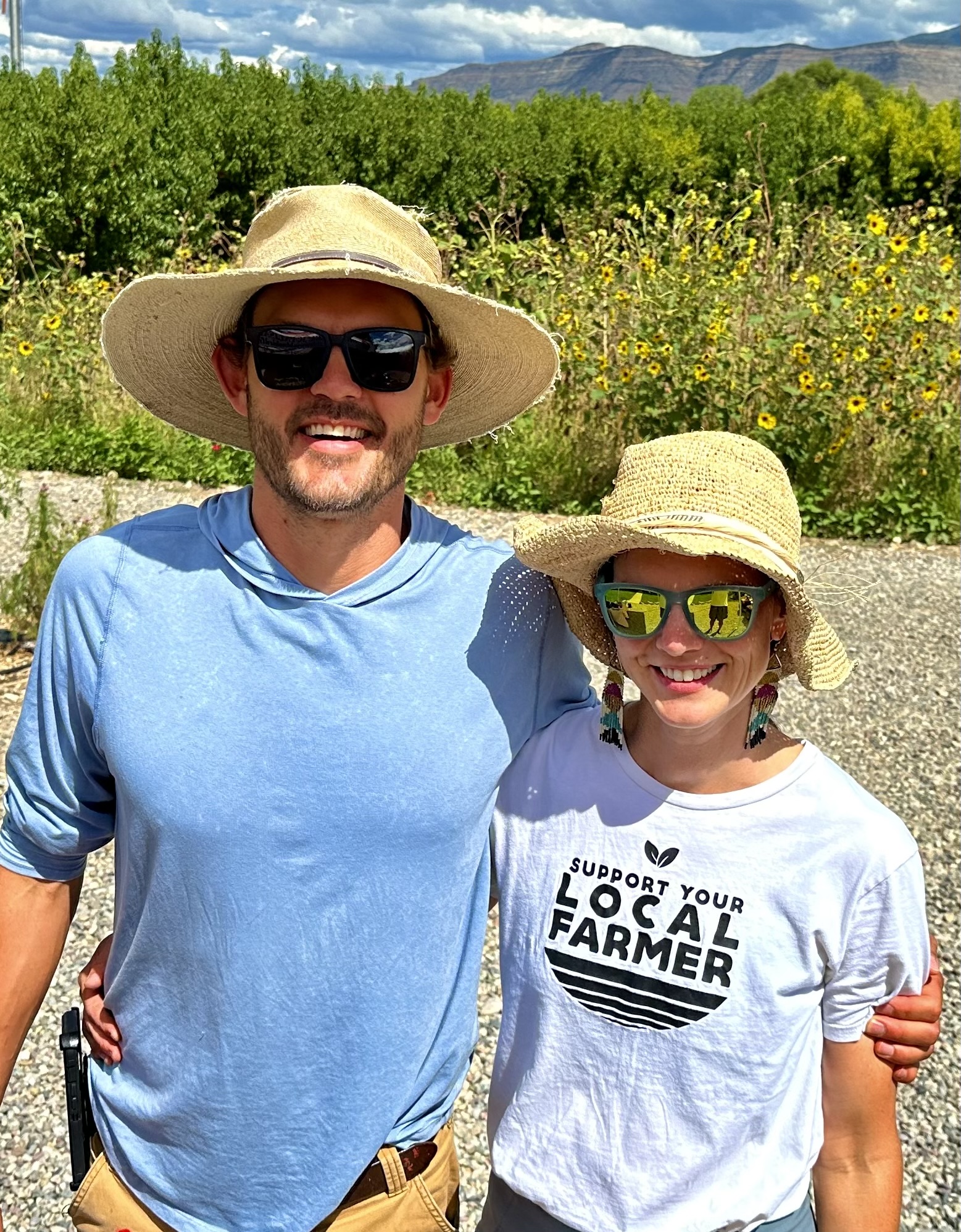 A man in a blue shirt and hat, left, standing with his arm around a woman in a white tshirt and hat