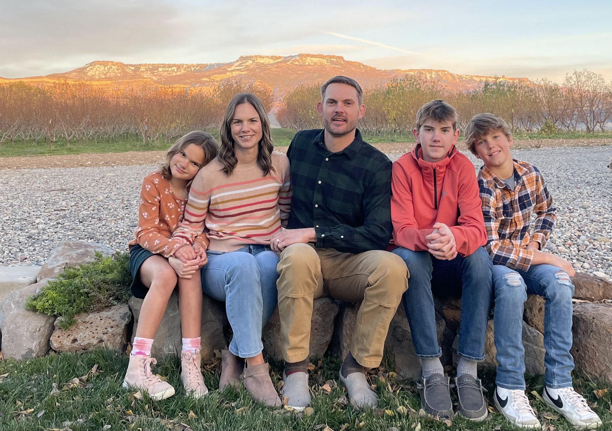 A family photo with (from left to right) a little girl, the mother, father, and two young boys perched on a rock