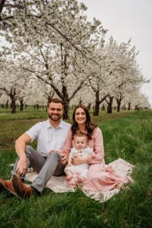 Cherry Ke’s Talon Falker with wife Mason and son Casen sitting on ground in front of a cherry orchard.