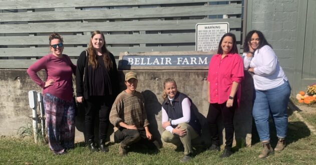 Six women posing in front of sign for Bellair Farm.