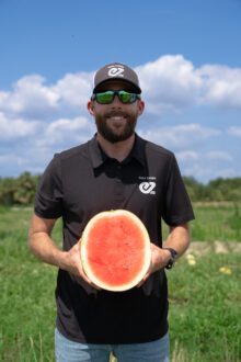 NASCAR racer and watermelon grower Ross Chastain holding a watermelon in a field.