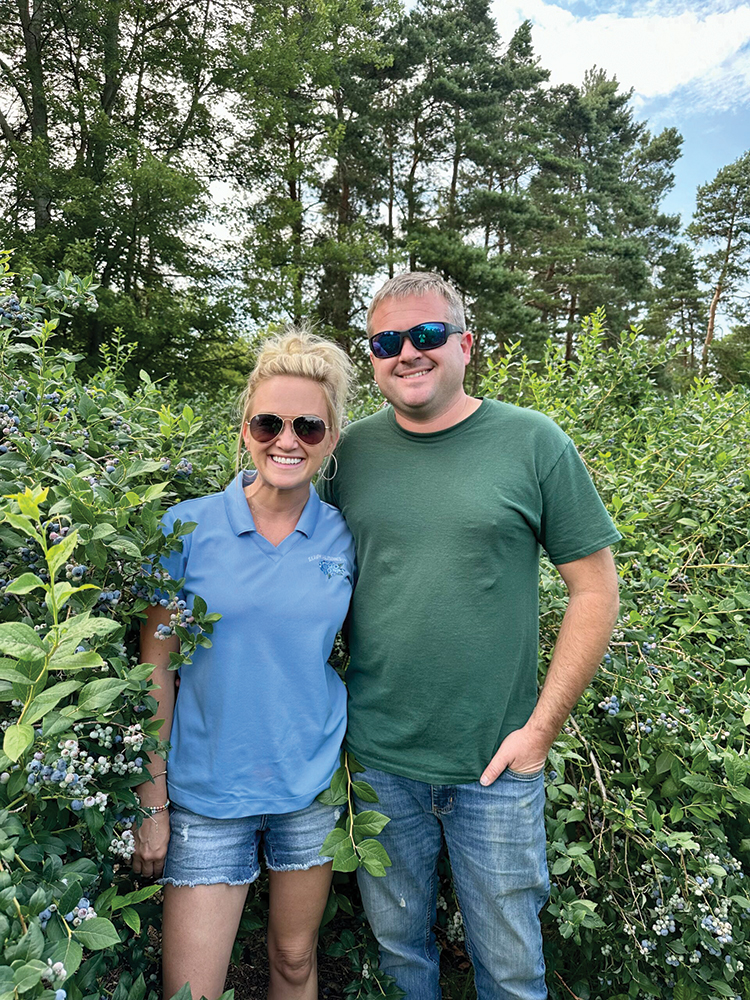 Blonde woman in a blue tshirt, left, standing with a blonde man in a green tshirt in a field