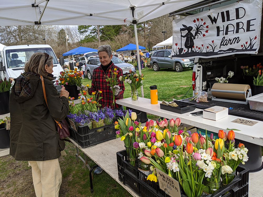 Farmer Leah Cook of Wild Hare Farm demonstrates what she calls the market's new "purchasing in a pandemic" policy as she has customers point to what they want so that she can pull the order together.