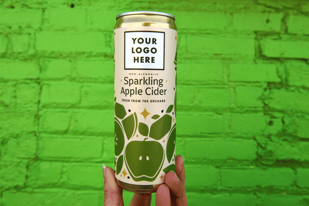 Green brick wall background in front is a hand holding up a can of sparkling apple cider that says "your logo here"